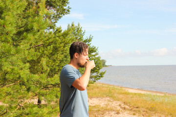 young man in t-shirt drinking morning coffee in a cup in nature and looking at the sea. hiking and camping concept.