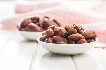 Almond nuts coated in sugar and honey in bowl on white table.