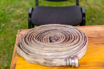 coiled fire hose with metal couplings placed on a wooden table, likely as part of an outdoor...