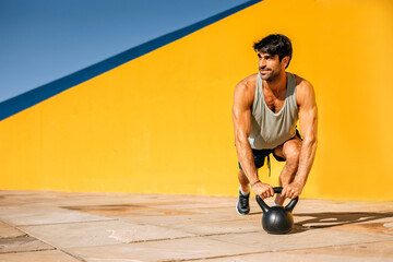 Hispanic athlete exercising with a kettlebell against a vibrant backdrop on a sunny day