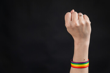 Woman with wedding ring and rainbow bracelet holding fist on black background. 