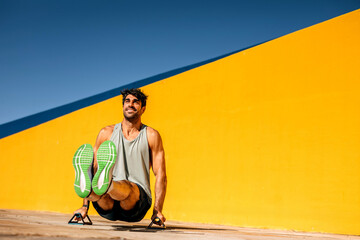 Hispanic athlete performs workout on outdoor gym equipment against vibrant yellow wall under clear...