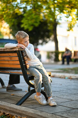 A boy sits on a bench in a quiet town on a warm day. A peaceful moment in the heart of a small...