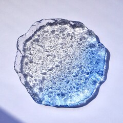 Decorative clear blue glass plate object isolated on square paper background from top angle view.