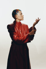 Woman with colorful hair wearing a red leather coat poses gracefully against a minimalist white...