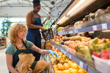 Grocery store workers arranging fresh fruits on display shelf