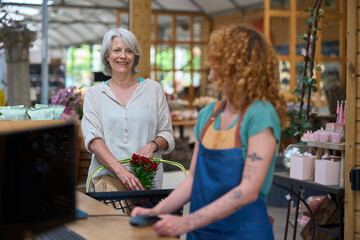 Senior woman buying flowers at garden center checkout: paying using contactless technology