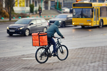 Fast food courier on bicycle riding through the streets in cold weather, timely delivery while navigating urban traffic. Delivery worker on bicycle transporting food orders. Man delivering pizza.