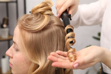 Fototapeta premium Hairdresser curling woman's hair in salon, closeup