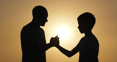 Father and son shaking hands outdoors, close-up of hands against soft sunlight. Father shaking...