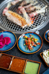 A table with plates of various foods, sauces, and a grill