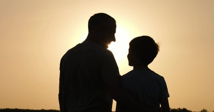 Father hug son during peaceful sunset. Father and child hug in golden light as silhouettes blend into sky. Father expresses love and care in quiet emotional connection outdoors.