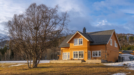 Panorama with yellow single house on beach of North Atlantic. colored hotel,  wooden holiday home on the islands Kval&oslash;ya. yellow grass on shore of the ocean and snowy mountains in background