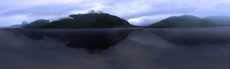 A panoramic photo shows mountains reflected in the waters of the Straight of Magellan