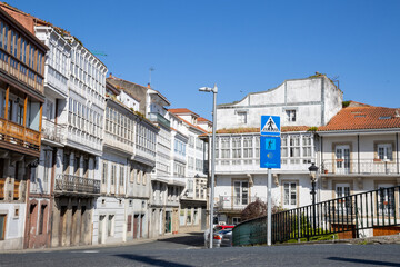Obraz premium Traditional Galician white buildings seen from Ponte Vella bridge over Mandeo River in Betanzos, Spain, surrounded by lush greenery.