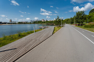 Fototapeta premium In the peaceful scene, there exists an empty road that features a beautiful wooden walkway, complemented by a serene lake visible in the background, enhancing the tranquil atmosphere