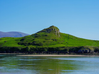 A small green hill rises above the calm water with a narrow path leading to the top