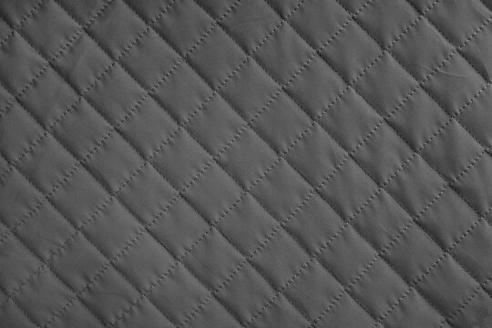 Checkered, diamond stitching pattern, black quilted fabric background. Blanket or puffer jacket, stitch rhombus texture close up, macro. Wallpaper, backdrop.