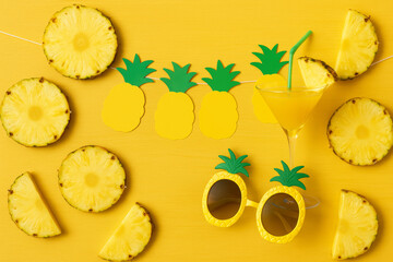 Tropical party flat lay with pineapple slices, sunglasses, juice, and paper garland – yellow summer celebration and fruity cocktail concept

