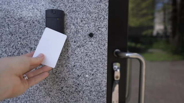 Modern access control concept. Close-up of female hand using access key card on smart door entry device. Red light changes to green. Glass door, granite wall background. Office security in action.