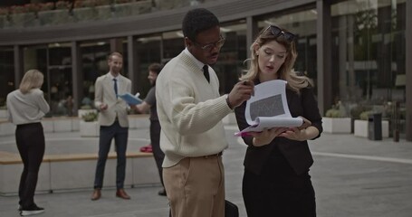 A diverse business team collaborates on a project, reviewing documents and discussing strategy in a modern urban setting. - Powered by Adobe