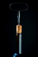 Opening a glass wine bottle with corkscrew on black background, closeup