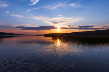 Tranquil sunset view over a calm lake with reflections of the plants and forest