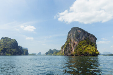 Obraz premium serene view of towering limestone cliffs surrounded by calm emerald waters, showcasing lush greenery and a clear blue sky on a sunny day in a tropical coastal region