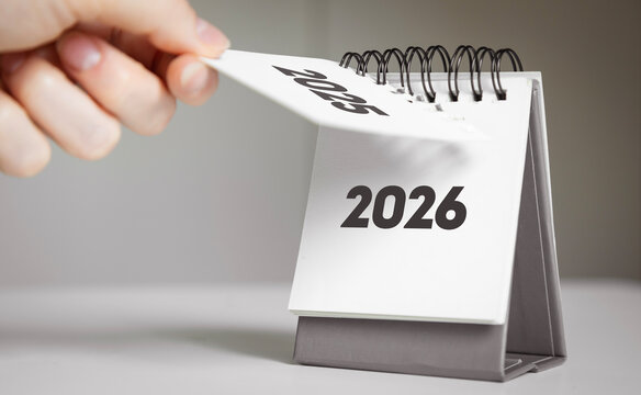 Turning the page from 2025 to 2026 – New Year calendar concept with hand and desk flip calendar