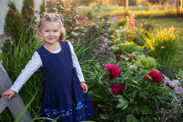 cheerful 3-year-old girl in a blue dress walks near the flowering flower bed in the backyard