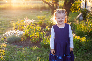 cheerful 3-year-old girl in a blue dress walks near the flowering flower bed in the backyard