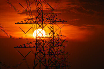 Silhouette of high-voltage electric transmission pole with big sun in the background during sunset