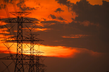 Silhouette of high-voltage electric pole with red-orange clouds during sunset with copy space