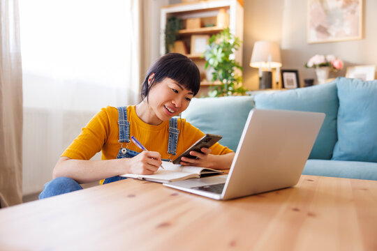 Woman using smart phone and taking notes while working from home