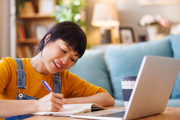 Woman taking online course using laptop computer and writing notes