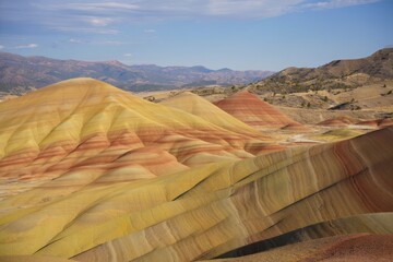Colorful layered hills with smooth contours under a clear blue sky in a dry landscape with distant mountains