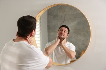 Handsome man looking at himself in mirror indoors