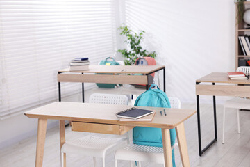 Empty classroom with wooden desks, chairs and backpacks