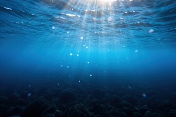 Underwater scene with deep blue water illuminated by sunlight beams penetrating the ocean surface over rocky seabed creating a peaceful and serene atmosphere