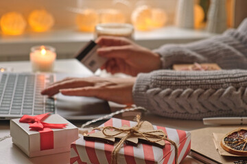 Woman using laptop and credit card, making online purchases at cozy home. Holiday shopping. Gift...