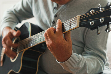 Senior man is playing guitar. Elderly male sitting at sofa and play music. Portrait of a gray...