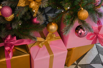 Big Wrapped Gift Boxes Is Under the Christmas Tree. Pink and Gold Gift-Wrapped Box with Ribbon for Friends, Relatives. Close up. Packaging of Xmas Presents. Festive Decorations. Preparing for Holidays