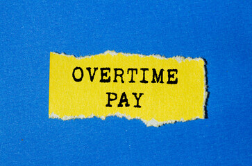 Overtime pay message written on ripped torn yellow paper on blue background. Conceptual overtime pay symbol. Copy space.