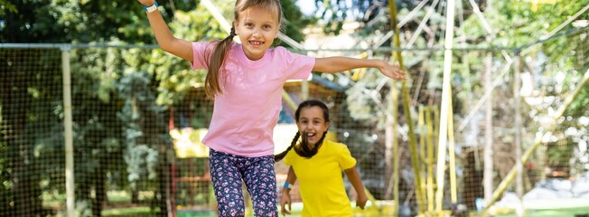 Pretty girls jumping together on colorful trampoline at playground park. Two sisters having fun during active entertainments 