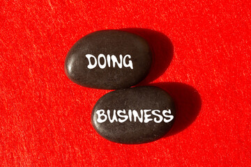 Doing business message written on black stones on red background. Conceptual doing business symbol....