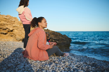 Two Women Relax on a Rocky Beach Facing the Sea in a Peaceful Setting