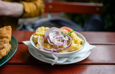 Traditional potato salad with red onions served in bowl on wooden table outdoors