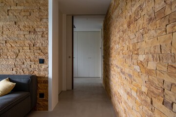 Modern interior hallway with textured natural stone walls, minimalist gray sofa with beige pillow, and a clean, serene atmosphere