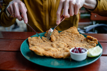 Breaded schnitzel with cranberry sauce and lemon slice on a green plate on a wooden outdoor table