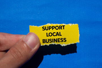 Support local business message written on ripped torn yellow paper piece on blue background. Conceptual support local business symbol. Copy space.
